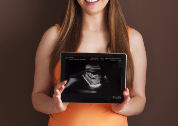 Beautiful pregnant woman showing ultrasound scan on digital tablet الأسئلة الشائعة